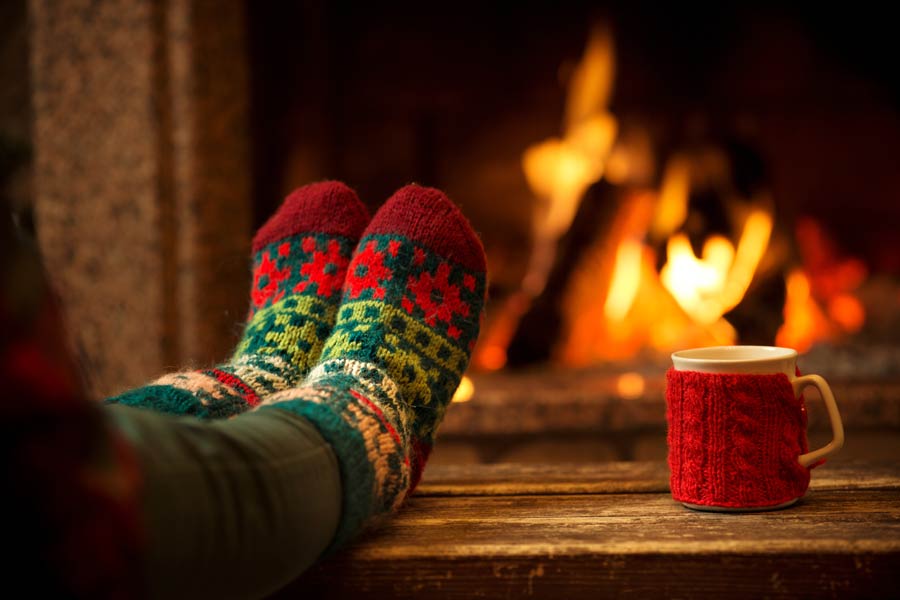 Someones feet, with Christmas socks, warming in front of the fireplace, with a cup on the side.
