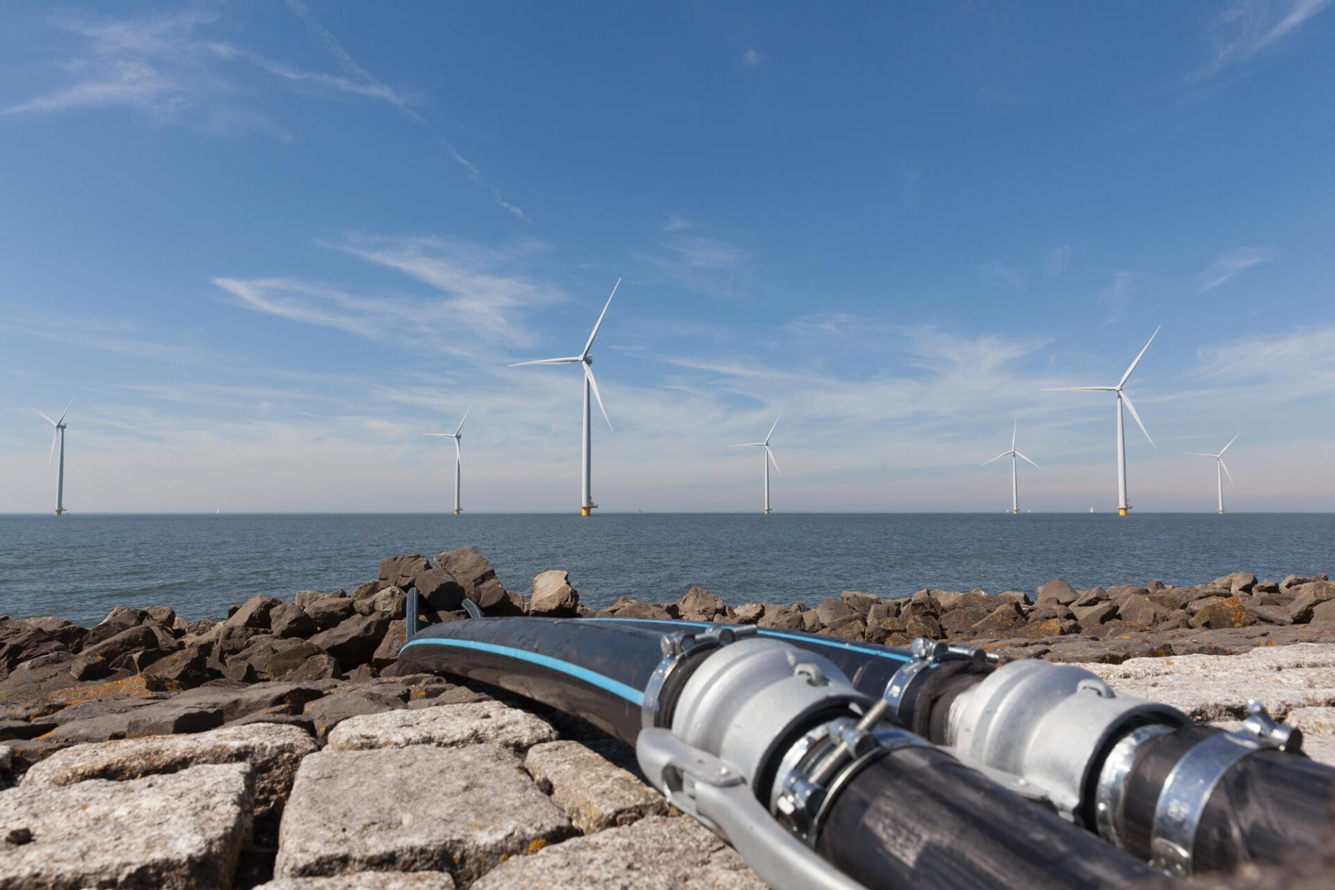 Shoreline with subsea cables in the foreground and offshore wind turbines and the background.