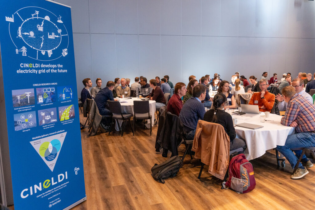 workshop der mennesker sitter rundt bord og samarbeider, med CINELDI-roll-up i forgrunnen
