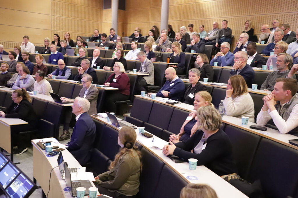 En gruppe mennesker deltar på en konferanse i en auditorium.