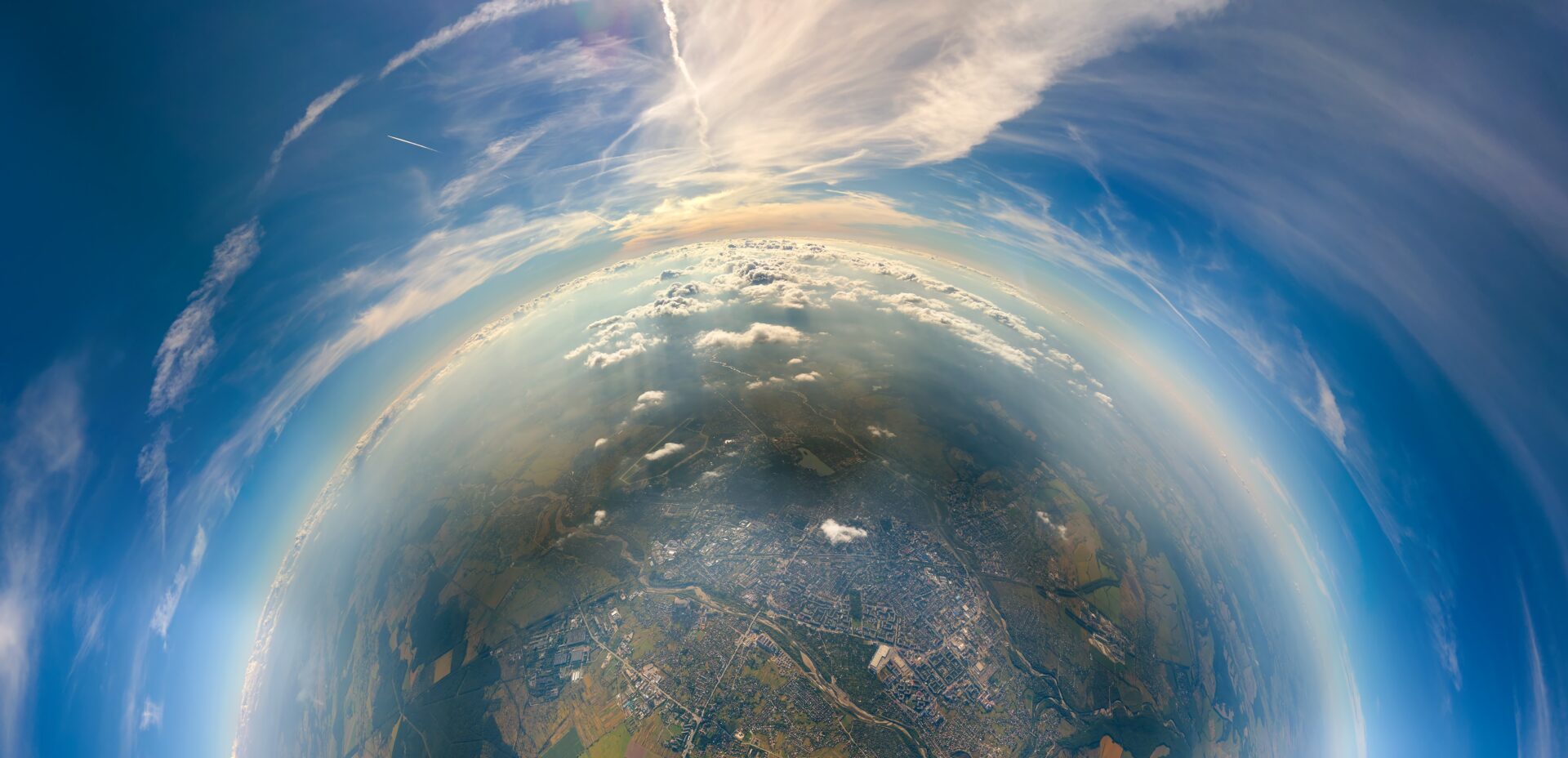 Aerial view from airplane window at high altitude of little planet distant city covered with layer of thin misty smog and distant clouds in evening