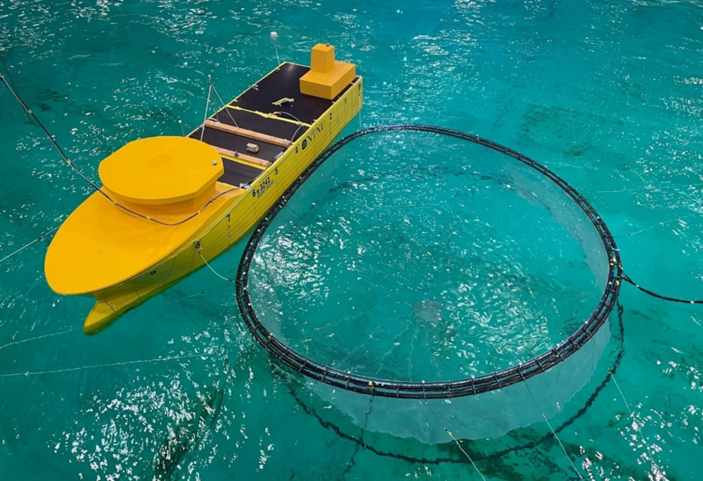 Gull modellbåt ved siden av merd i testbasseng.